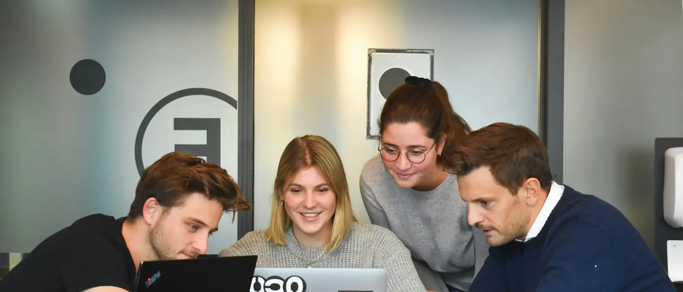 Vier Kolleginnen und Kollegen schauen gemeinsam auf einen Laptop